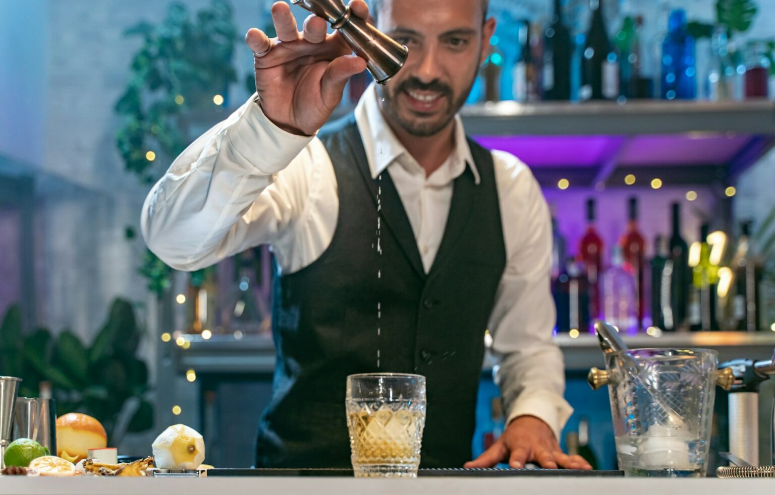 Combien rapporte une boîte de nuit par mois ? Expert barman in a white shirt and black apron smiling happy making cocktail at party in nightclub