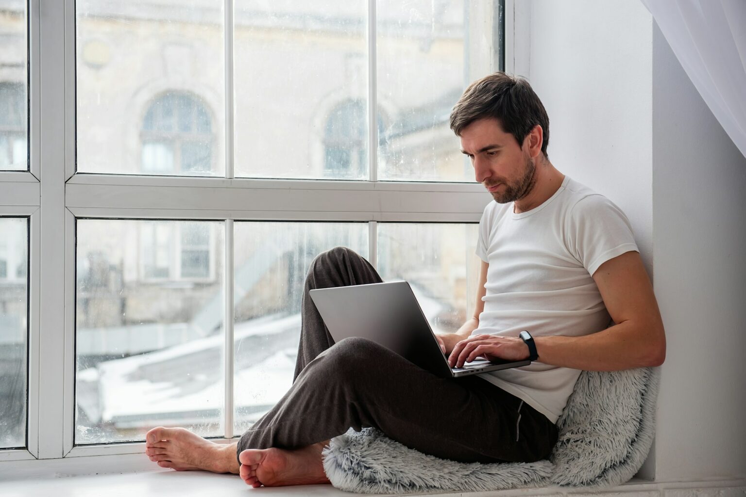 Comment désinstaller un logiciel ou une application sous Windows ? Young handsome man sits on wooden windowsill near the window in lotus position, works on gray laptop
