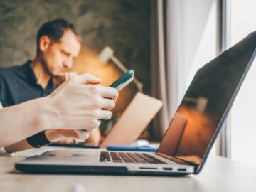 Businesswoman texts message on smartphone working on contemporary laptop
