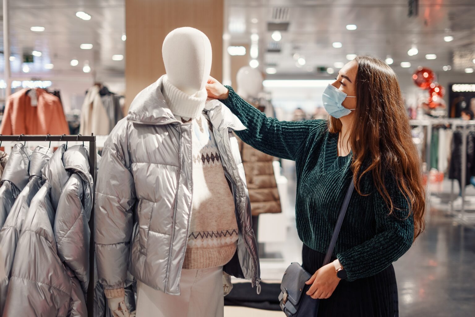 La Doudoune : Élégance et Chaleur au Féminin Young brunette lady in face mask chooses warm clothes during pandemic, buying puffy winter jacket