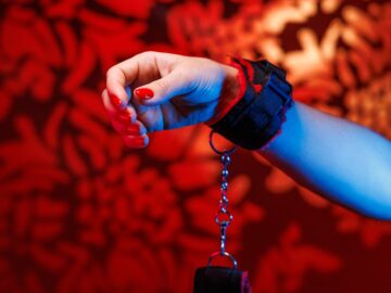 Soft BDSM handcuffs adorn a womans hands with alluring red nails