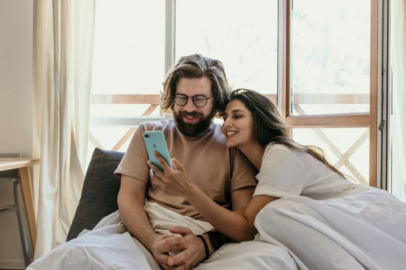 Content couple enjoying a leisure morning in bed, interacting with a smartphone.